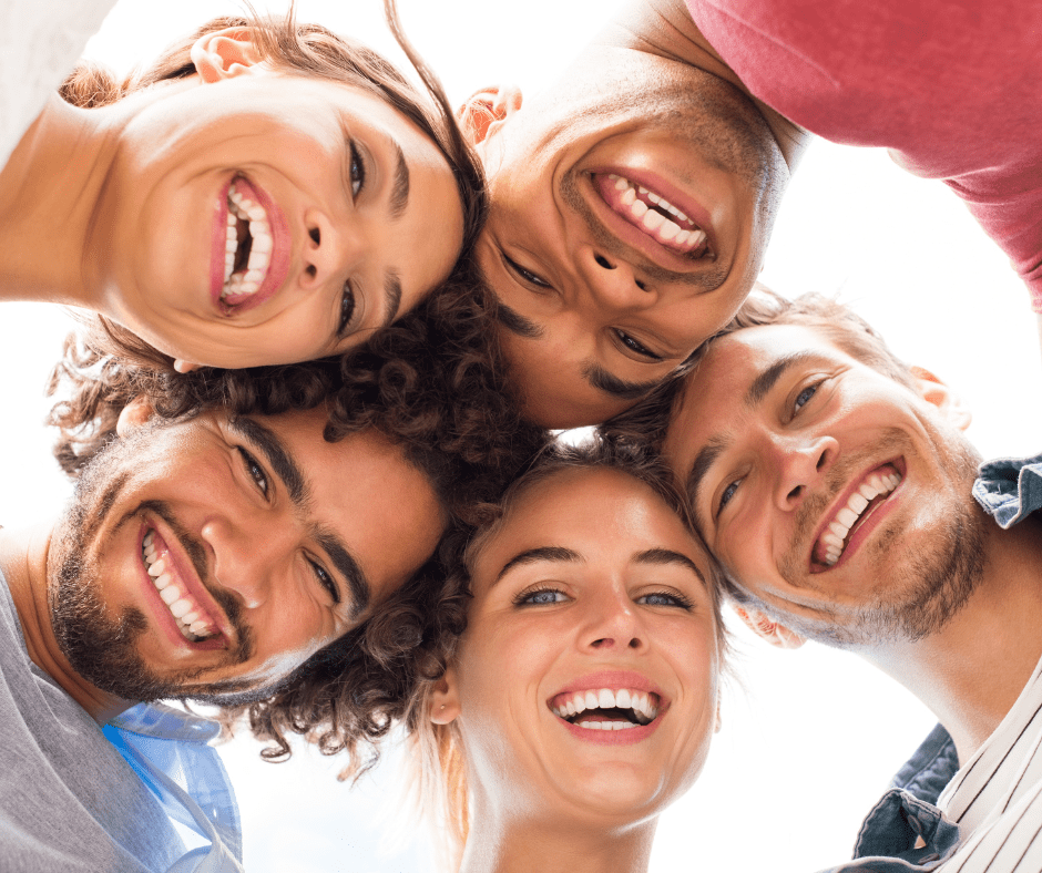 A group of friends with healthy smiles forming a circle, looking down into the camera, indicative of the care from a Dentist in Meridian